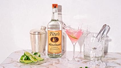 Tito's Handmade Vodka bottle and a cosmopolitan cocktail with a lime garnish