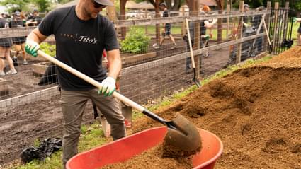 Man shoveling dirt into wheelbarrow wearing Love, Tito's t-shirt