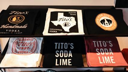 Two shelves with Tito's Handmade Vodka t-shirts