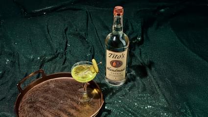 Tito's Handmade Vodka Bottle next to wooden tray and coup containing Tito's Pickle Martini with pickle garnish