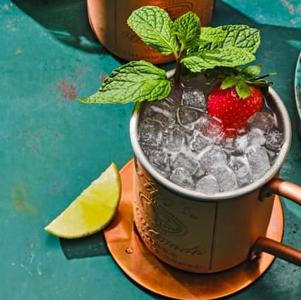 Tito's Handmade Vodka copper mug with Tito's Strawberry Mule cocktail garnished with strawberry and mint with lime wedges on the side