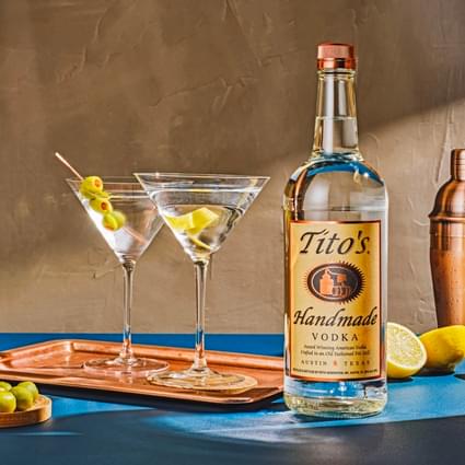Tito's Handmade Vodka bottle with copper cocktail shaker and two Tito's Martini cocktails with olive garnish