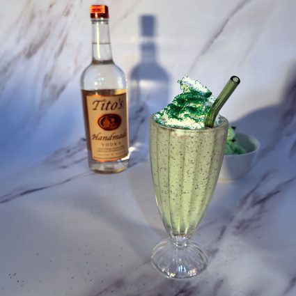 Tito's Clover Shake with whipped cream, green sprinkles and a straw with a bottle of Tito's Handmade Vodka