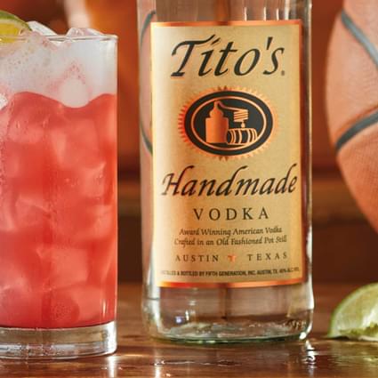 Tito's Handmade Vodka bottle and basketball next to Tito's Bay Breeze cocktail with lime wedge