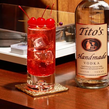 Tito's Handmade Vodka bottle next to Tito's Dirty Shirley cocktail garnished with three cherries